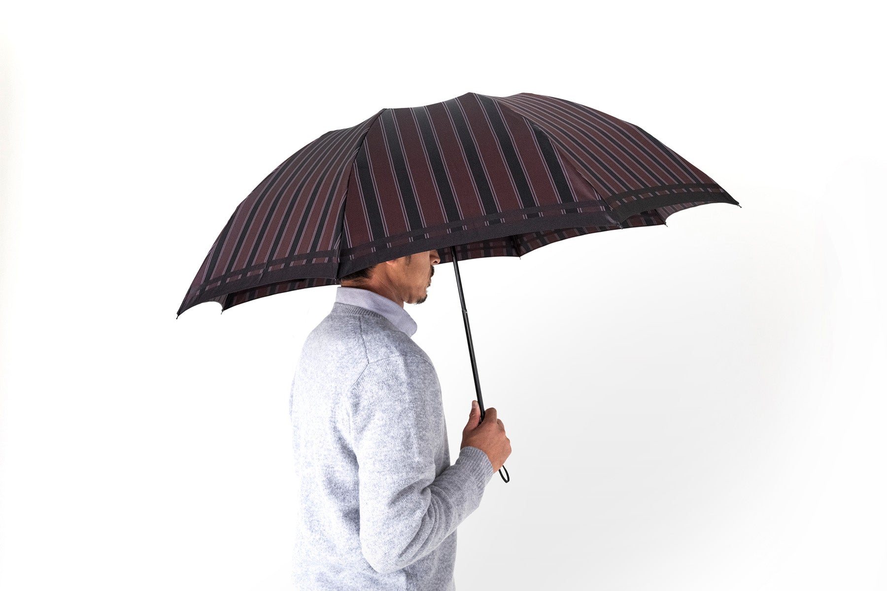 エンジ色のストライプ柄のメンズ折りたたみ傘を差す男性