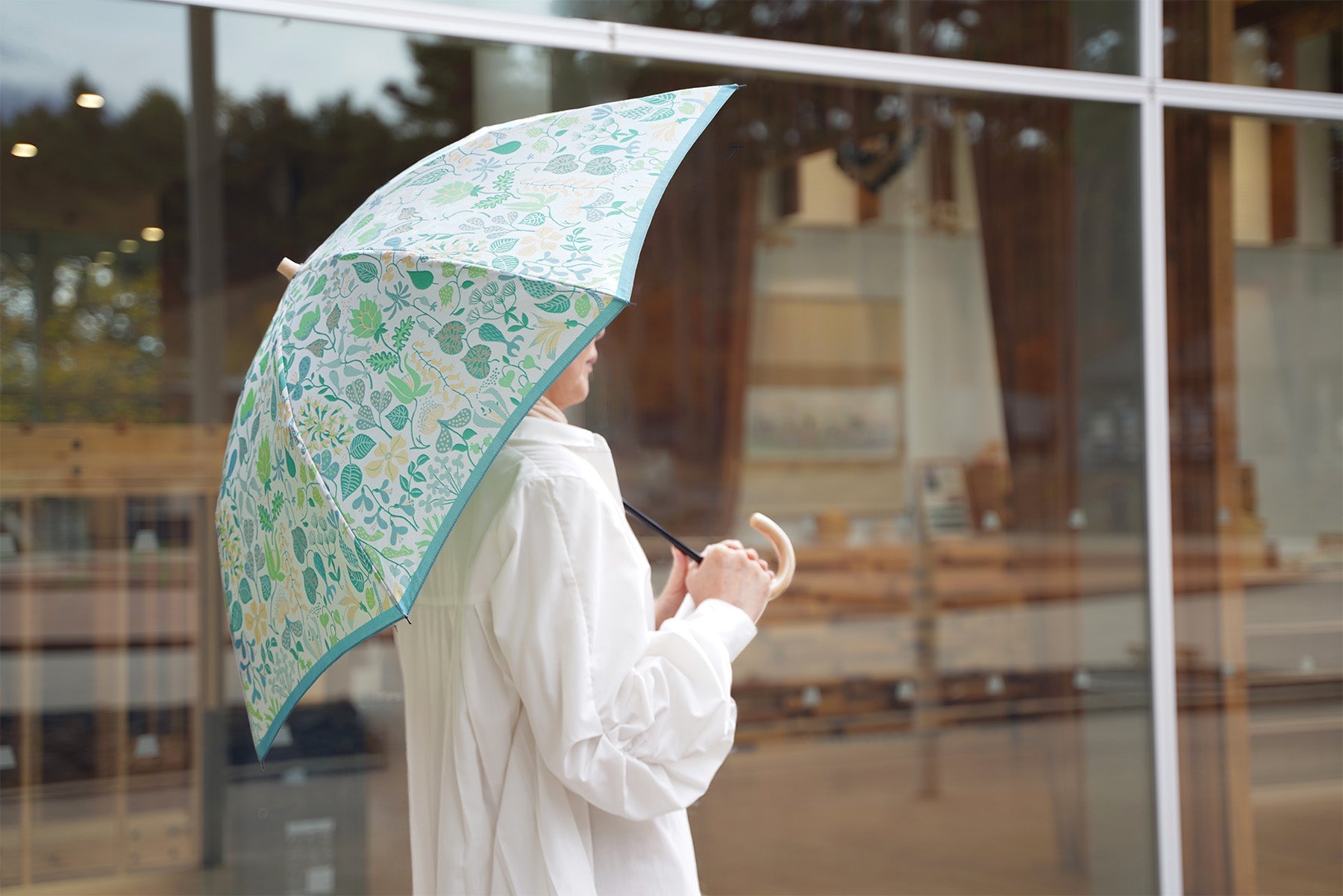 明るいグリーンの植物柄の晴雨兼用折りたたみ傘を差す女性