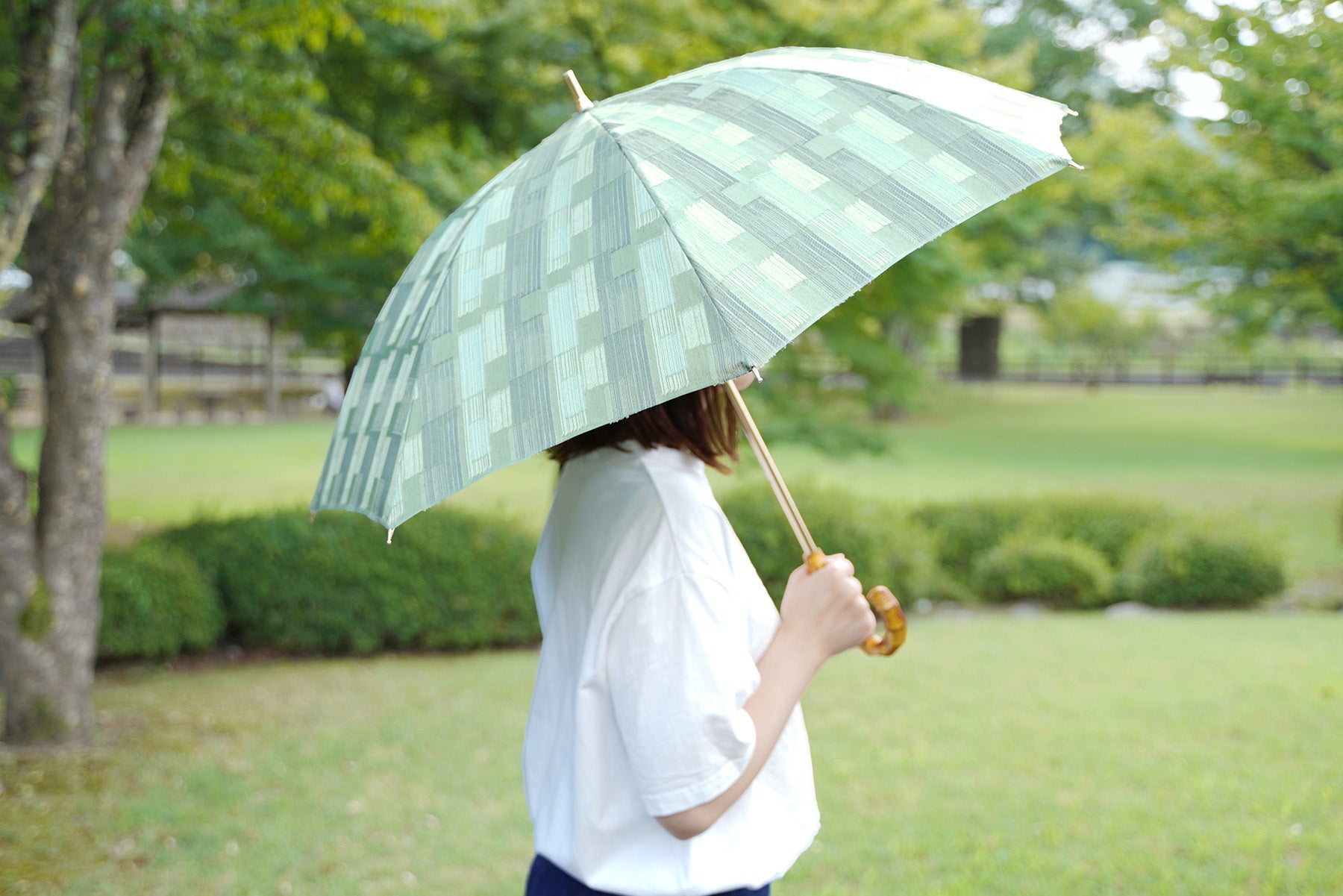 薄グリーンの晴雨兼用日傘を差す女性