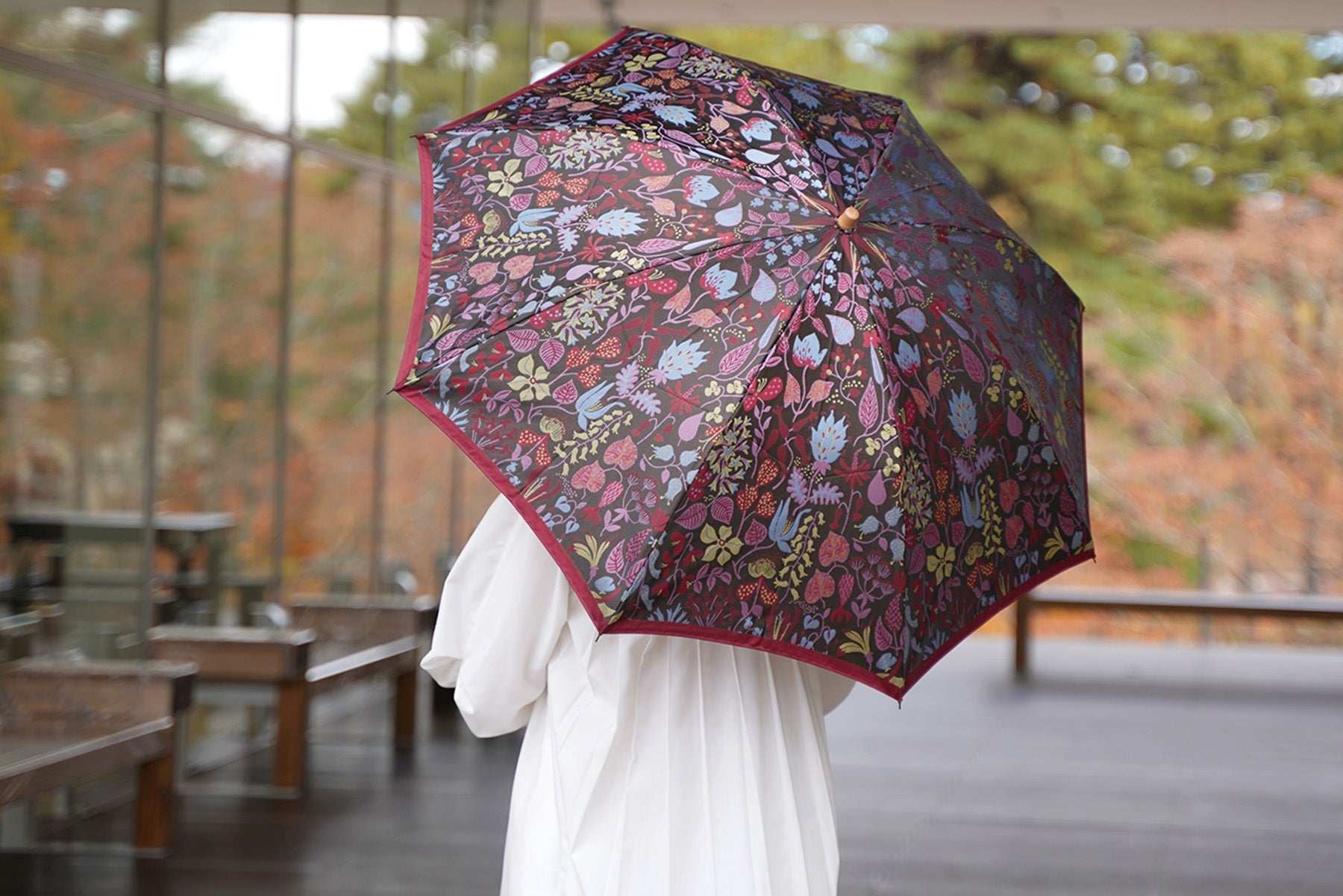 植物柄の赤い折りたたみ傘を差す女性